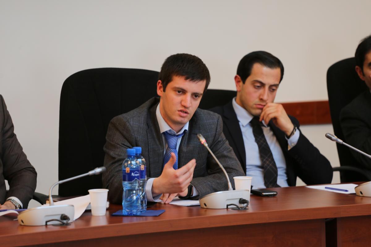 A white man in a suit talks into a microphone.